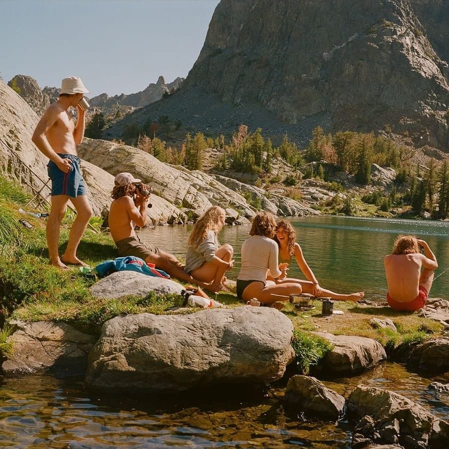 Seven friends resting on the rocks beside an alpine lake in the sunshine.